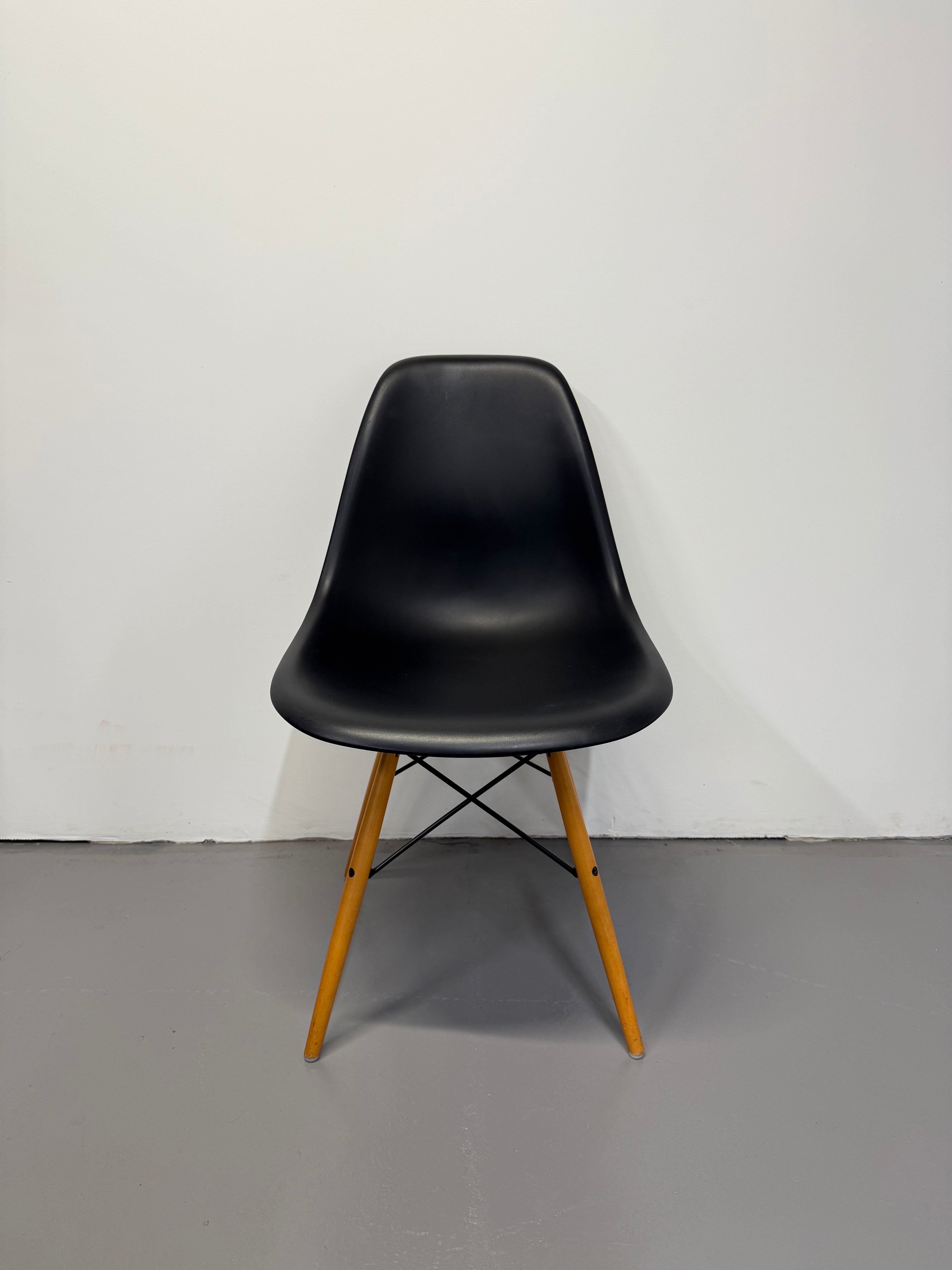 Black chair with wooden legs on a white floor and gray wall