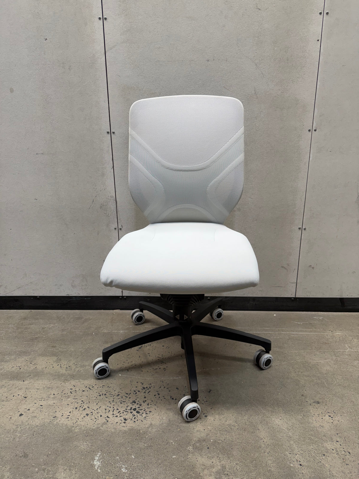 A modern white ergonomic office chair with a black five-star wheeled base, positioned against a concrete wall and floor.
