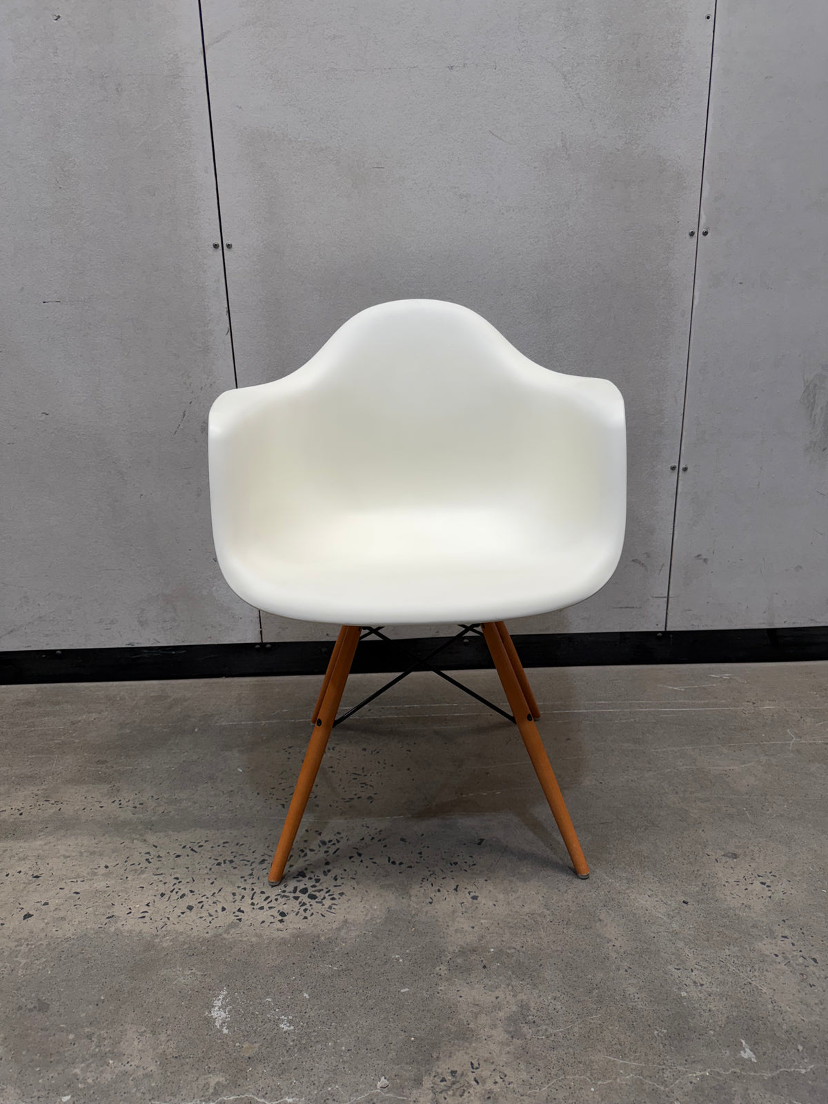 A modern molded plastic armchair with a white shell and tapered wooden legs, set against a gray concrete wall and floor.