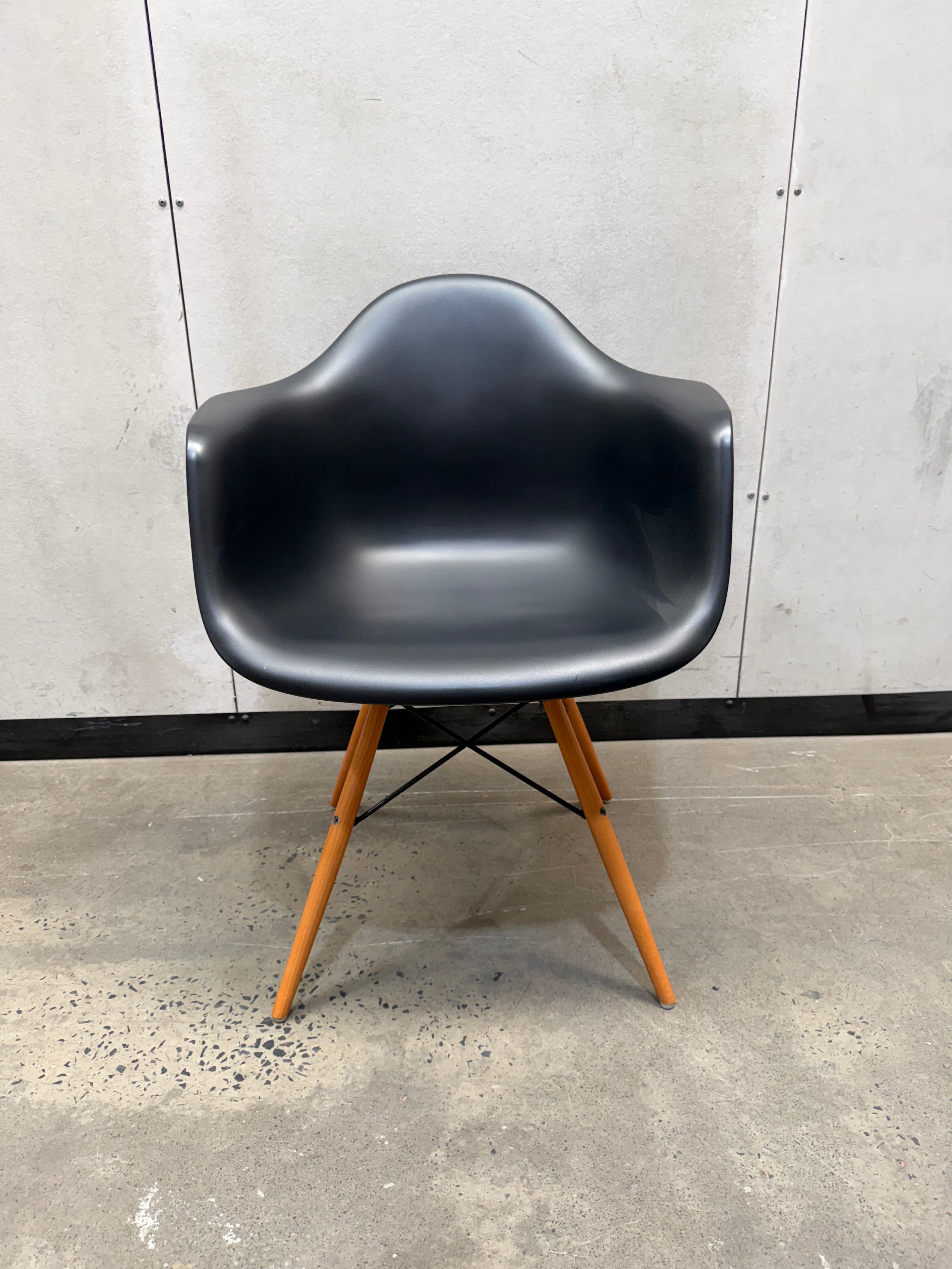A molded black plastic side chair with light brown wooden legs, positioned against a gray concrete wall and floor.