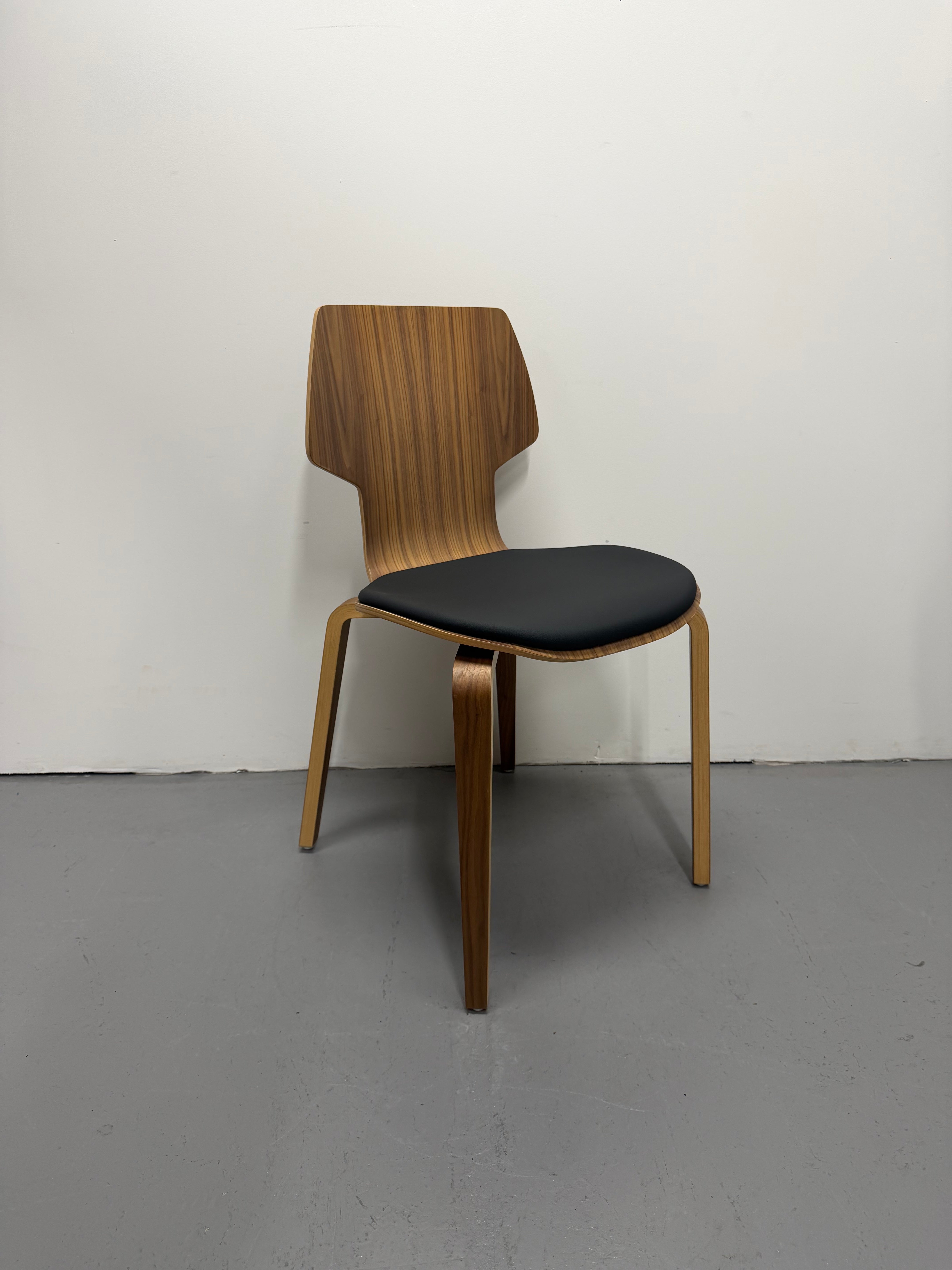 Wooden chair with a black seat against a white wall