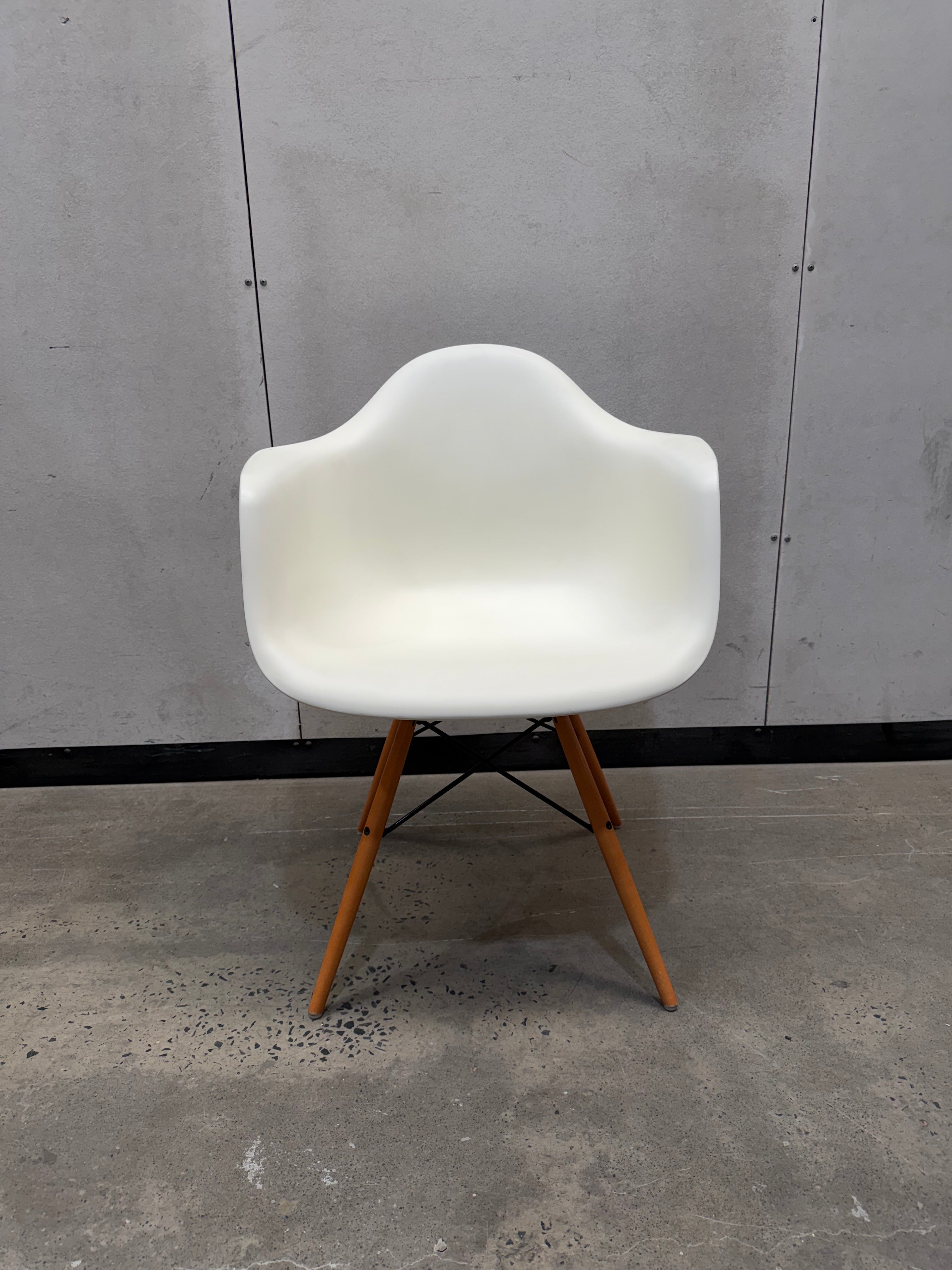A modern molded plastic armchair with a white shell and tapered wooden legs, set against a gray concrete wall and floor.